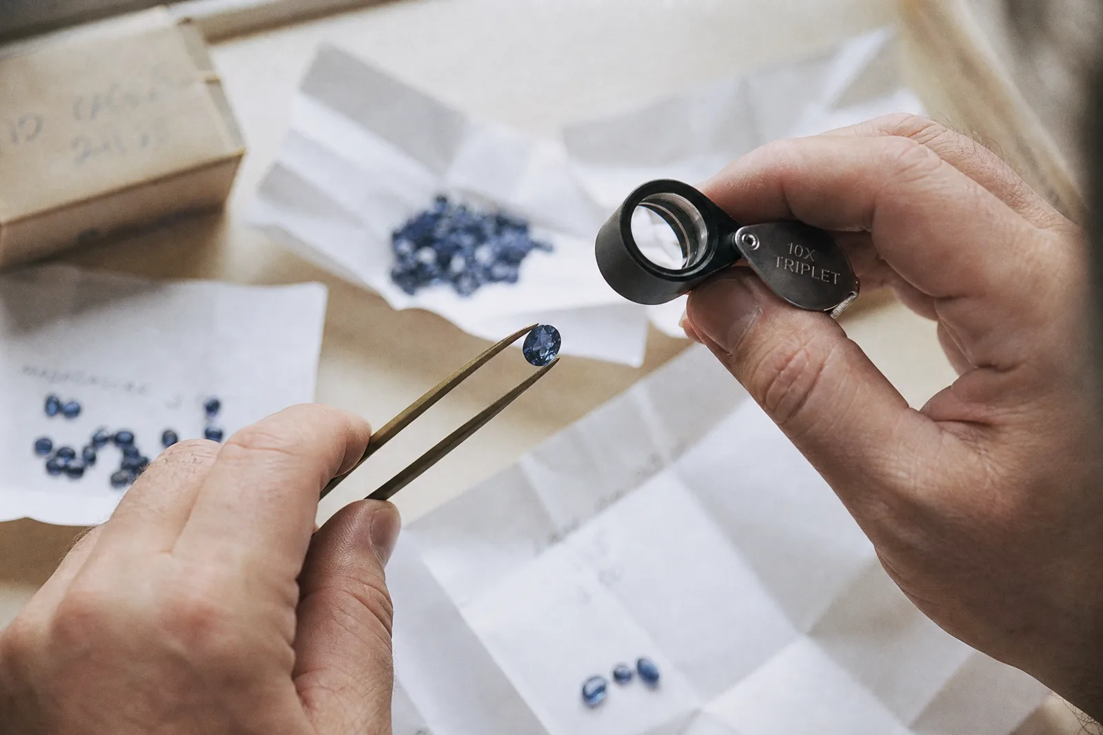Grading a blue sapphire with tweezers and a 10x loupe over sorting paper